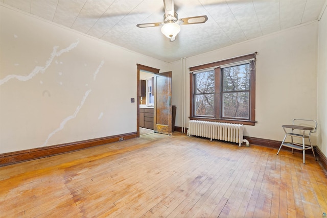 empty room featuring baseboards, ceiling fan, light wood-style flooring, and radiator