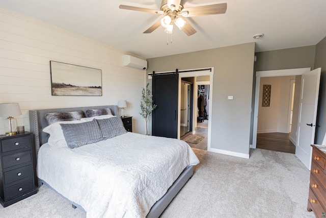 bedroom with a walk in closet, light colored carpet, a wall mounted AC, a barn door, and wooden walls