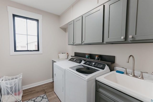 washroom with washing machine and dryer, cabinet space, a sink, baseboards, and light wood-style flooring