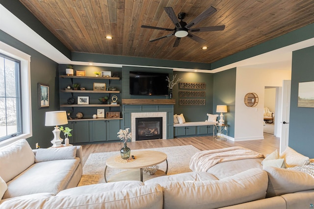 living area featuring a glass covered fireplace, baseboards, ceiling fan, wood ceiling, and light wood-style flooring