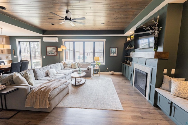 living area with a raised ceiling, a glass covered fireplace, a ceiling fan, wooden ceiling, and a wall unit AC