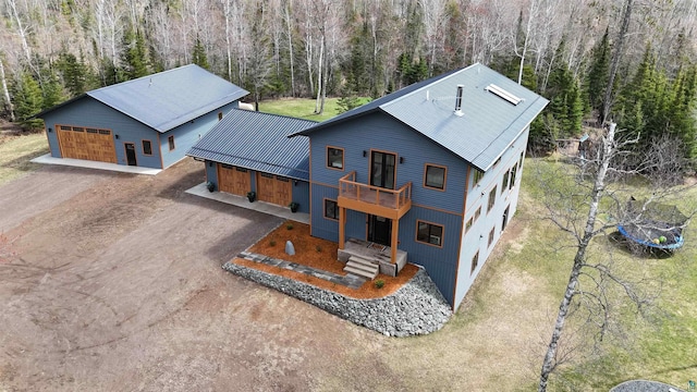 exterior space with metal roof, dirt driveway, a detached garage, a wooded view, and a balcony