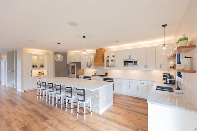 kitchen featuring a kitchen breakfast bar, appliances with stainless steel finishes, custom range hood, and light wood-type flooring