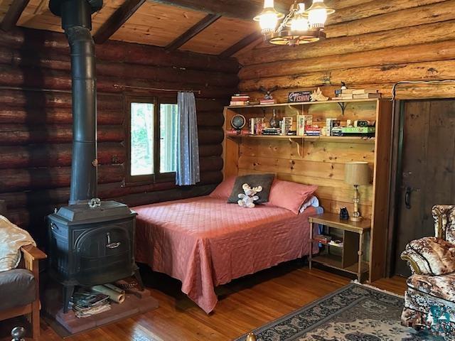 bedroom with a wood stove, wood finished floors, wooden ceiling, log walls, and vaulted ceiling with beams