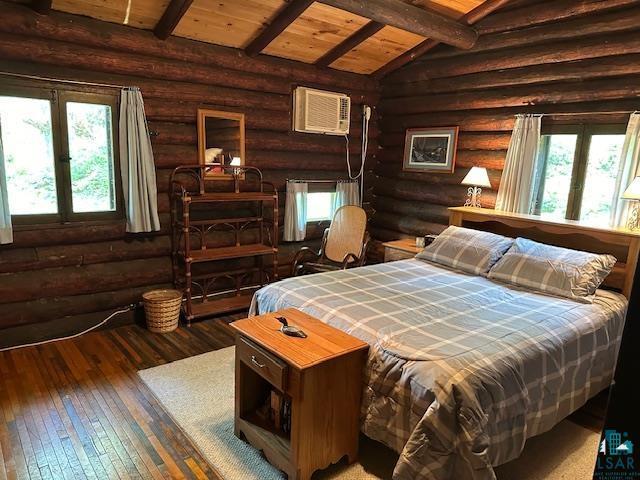 bedroom with log walls, hardwood / wood-style floors, a wall unit AC, wooden ceiling, and lofted ceiling with beams