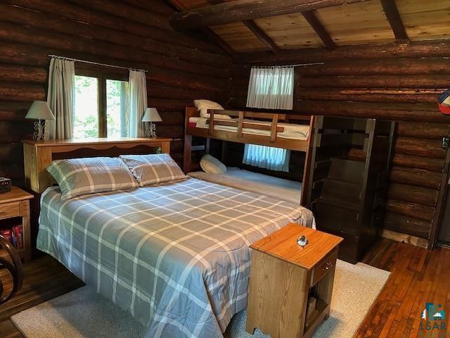bedroom featuring lofted ceiling with beams, wooden ceiling, rustic walls, and wood-type flooring