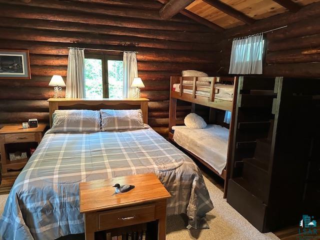 bedroom with carpet floors, vaulted ceiling with beams, rustic walls, and wood ceiling