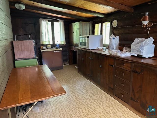 kitchen with dark brown cabinetry, brick patterned floor, wooden ceiling, white microwave, and beamed ceiling