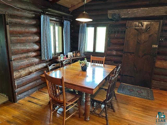 dining space with rustic walls, beam ceiling, and hardwood / wood-style flooring