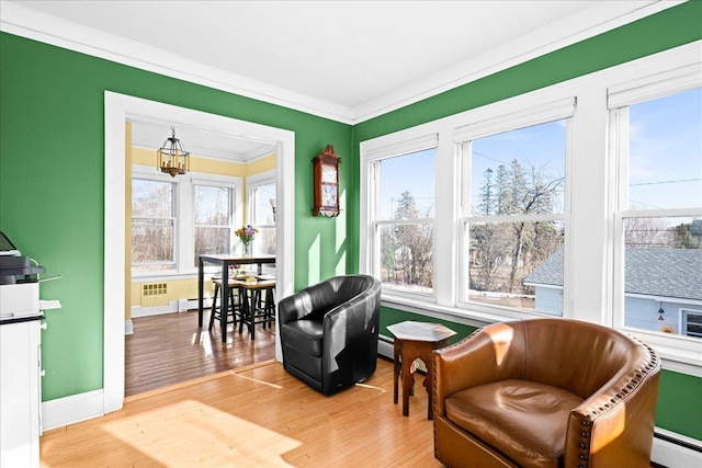living area with crown molding, baseboards, a baseboard heating unit, and light wood finished floors