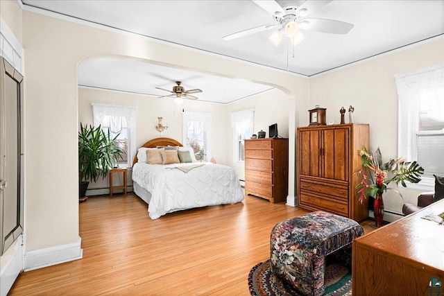 bedroom featuring arched walkways, ornamental molding, a baseboard heating unit, and light wood-style flooring