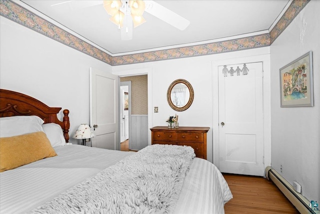bedroom featuring a ceiling fan, a baseboard heating unit, and wood finished floors