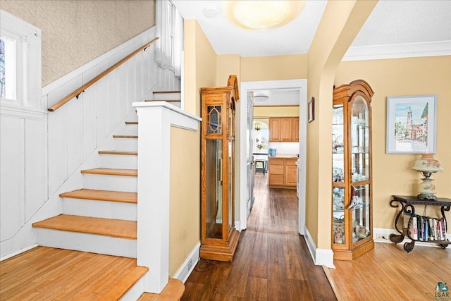 stairway with ornamental molding, wood finished floors, baseboards, a textured ceiling, and arched walkways