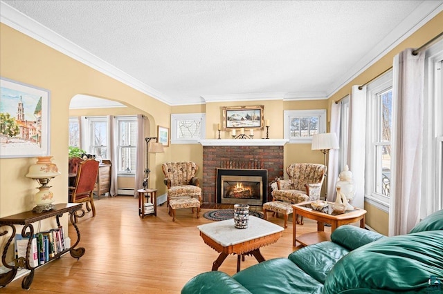 living area featuring ornamental molding, a textured ceiling, a baseboard heating unit, arched walkways, and light wood-style flooring