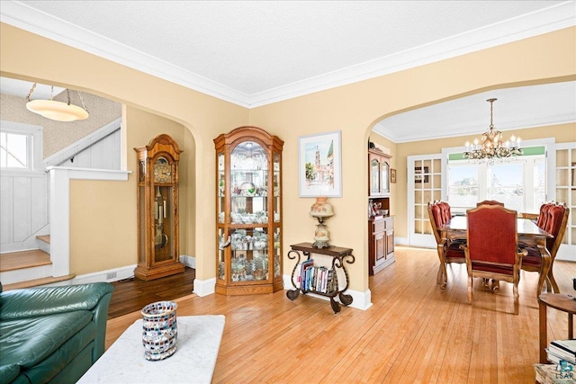 living area with arched walkways, light wood-type flooring, stairway, an inviting chandelier, and ornamental molding
