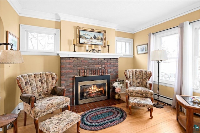 sitting room featuring crown molding, baseboard heating, a brick fireplace, and wood finished floors