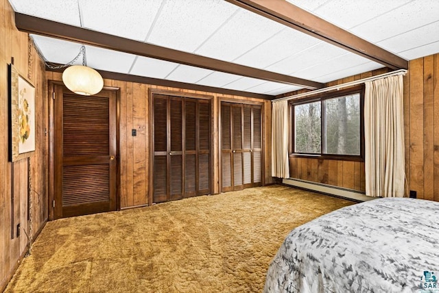 bedroom featuring beamed ceiling, a baseboard heating unit, wooden walls, multiple closets, and carpet flooring