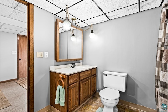 full bath featuring baseboards, a drop ceiling, toilet, and vanity