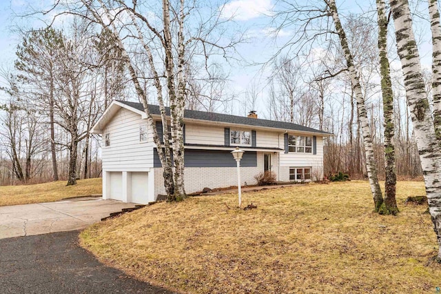 raised ranch featuring an attached garage, concrete driveway, a front lawn, and a chimney