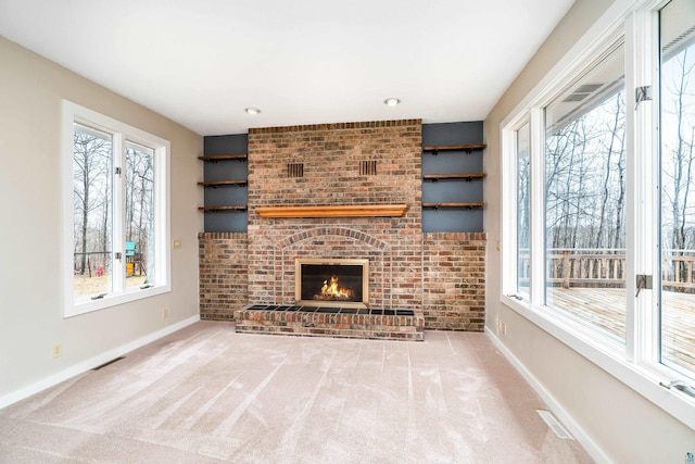 unfurnished living room featuring baseboards, carpet flooring, a brick fireplace, and a healthy amount of sunlight