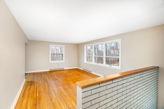 spare room with baseboard heating, wood finished floors, baseboards, a baseboard heating unit, and a wealth of natural light