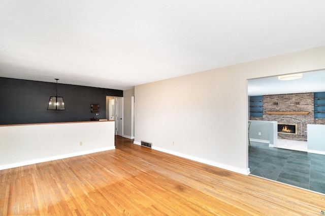 unfurnished living room featuring visible vents, wood finished floors, a fireplace, baseboards, and a chandelier