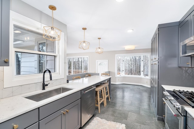 kitchen with appliances with stainless steel finishes, tasteful backsplash, a sink, baseboards, and gray cabinetry
