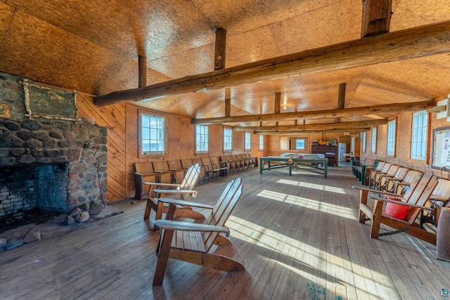 interior space with a stone fireplace, beam ceiling, and hardwood / wood-style floors
