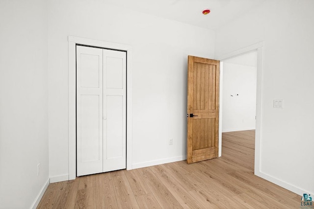 unfurnished bedroom featuring baseboards, light wood finished floors, and a closet