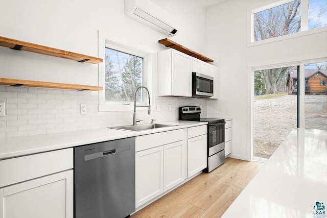 kitchen with open shelves, an AC wall unit, a sink, light wood-style flooring, and appliances with stainless steel finishes