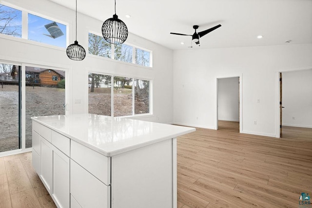 interior space featuring a kitchen island, baseboards, ceiling fan, white cabinets, and light wood-style flooring