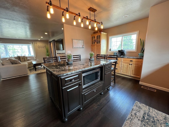 kitchen with visible vents, plenty of natural light, stainless steel microwave, and a kitchen bar