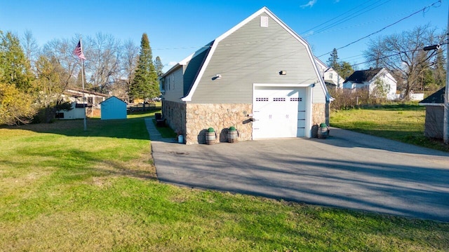 view of side of home with driveway, a lawn, a garage, a gambrel roof, and stone siding