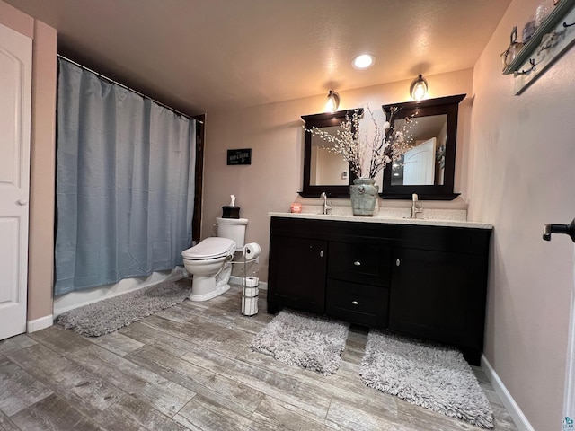 bathroom featuring double vanity, a sink, wood finished floors, and toilet