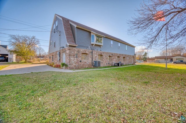 view of side of home featuring a gambrel roof, central AC, a yard, and stone siding