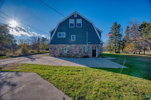 view of property exterior with a lawn, a patio area, a gambrel roof, and stone siding