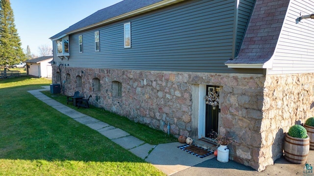 view of side of home featuring a lawn, fence, central AC, and stone siding