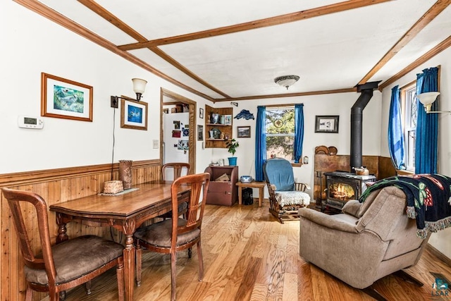 dining space featuring crown molding, wooden walls, a wood stove, light wood-style flooring, and a wainscoted wall