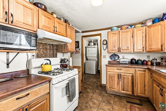 kitchen featuring gas range gas stove, stacked washer and dryer, under cabinet range hood, and dark countertops