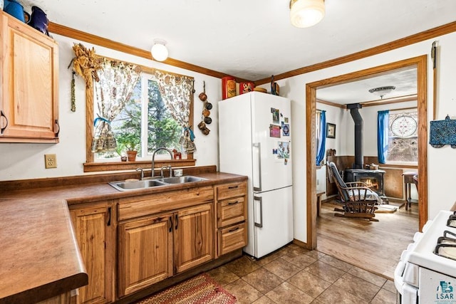 kitchen featuring tile patterned flooring, a wood stove, a sink, ornamental molding, and white appliances