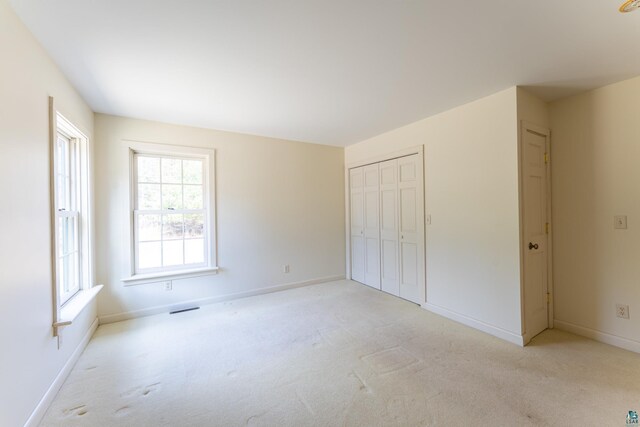 unfurnished bedroom with baseboards, visible vents, a closet, and light colored carpet