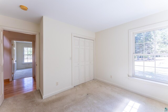 unfurnished bedroom featuring baseboards, a closet, and light colored carpet