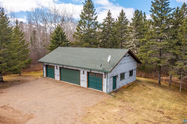 detached garage featuring a forest view and dirt driveway