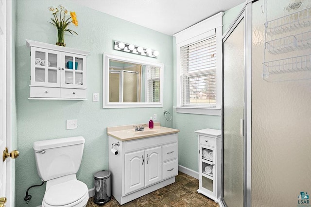 bathroom featuring vanity, toilet, baseboards, stone finish flooring, and a stall shower