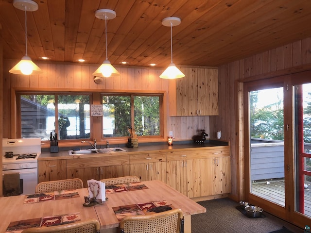 kitchen with light brown cabinetry, white gas range oven, a sink, wood walls, and wood ceiling