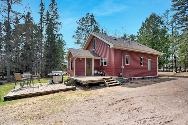back of house featuring roof with shingles and a wooden deck