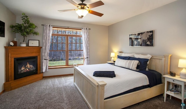 carpeted bedroom featuring baseboards, a ceiling fan, and a lit fireplace
