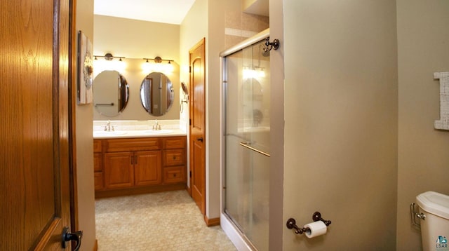 bathroom featuring double vanity, a sink, a stall shower, and toilet