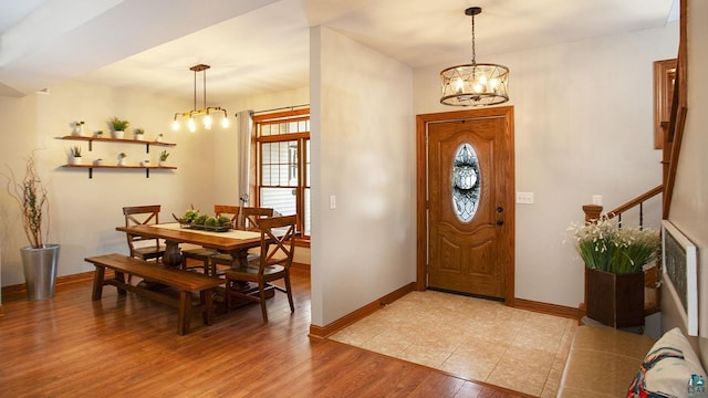 entrance foyer with stairs, baseboards, a notable chandelier, and light wood-style flooring
