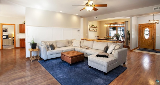 living room with ceiling fan, visible vents, dark wood-style floors, and a decorative wall